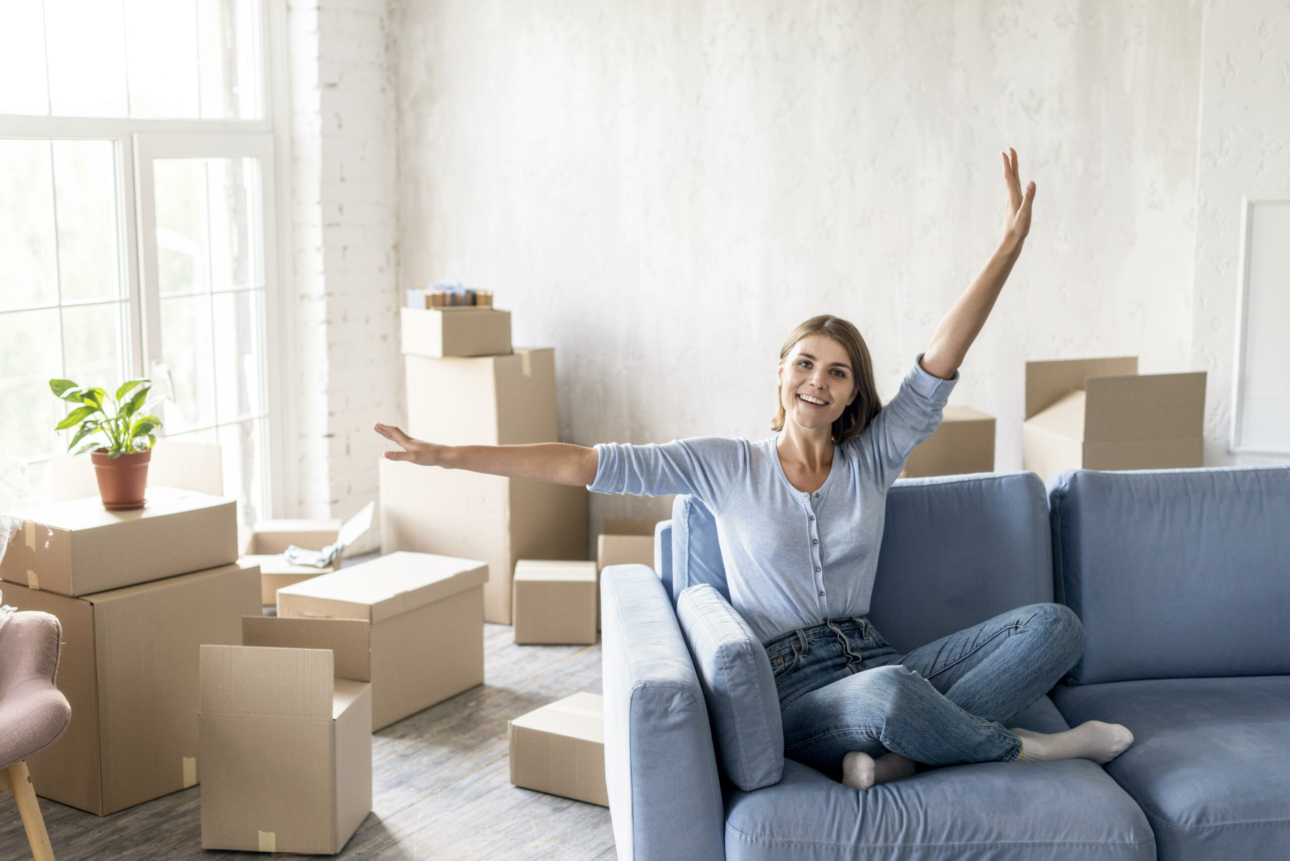 Sourire en living avec des cartons, une femme détendue sur un canapé bleu, ambiance déménagement et checklist déménagement à venir.
